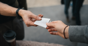 A man handing a folded handwritten note to another person outdoors, representing the quiet passing on of influence