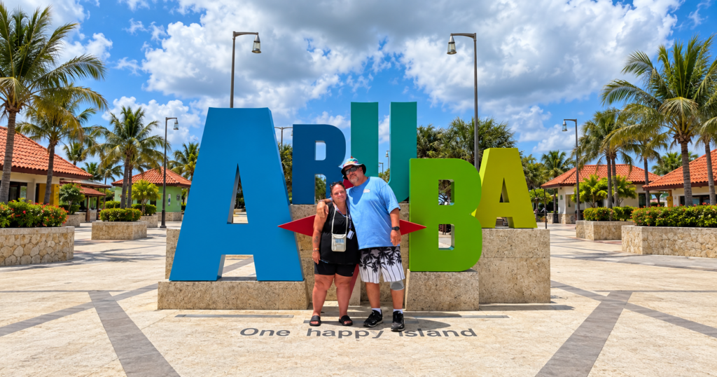Michael and Annita standing together at the colorful Aruba One Happy Island sign