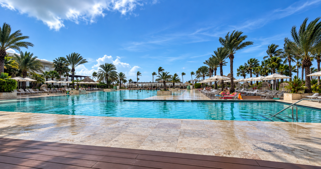 Turquoise resort pool surrounded by palm trees and lounge chairs in Curaçao